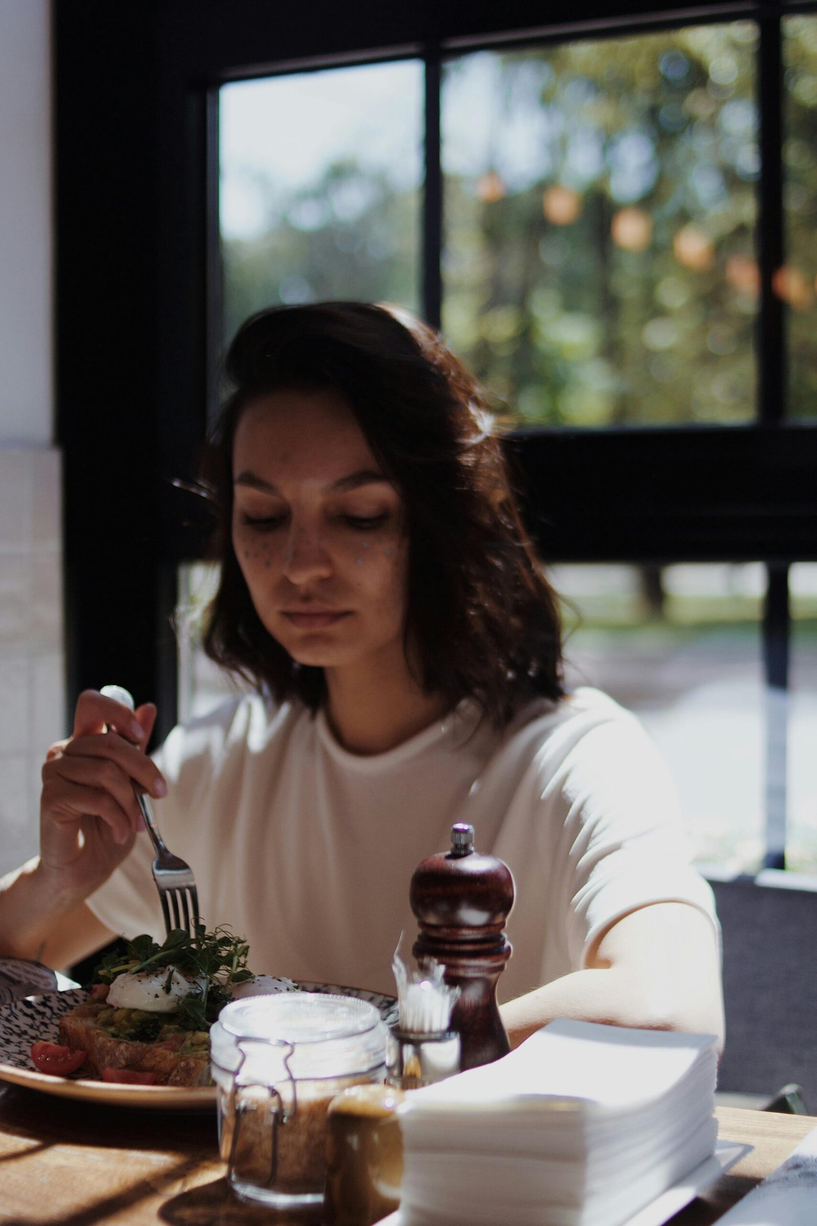 A woman seated alone enjoying a meal in a sunlit café, reflecting tranquility.