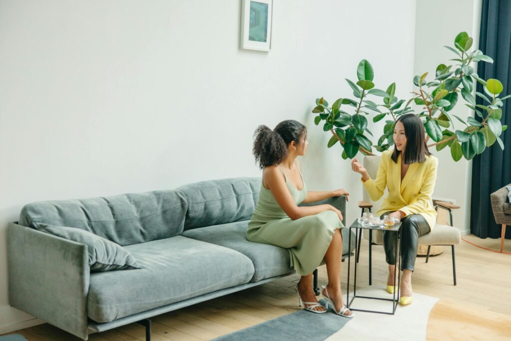 Two women sharing a conversation in a stylish living room with plants.